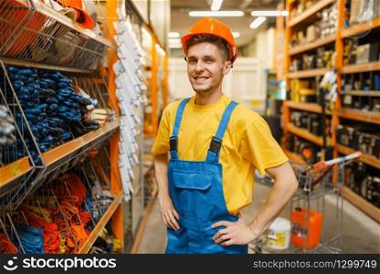 Male builder trying on helmet at the shelf in hardware store. Constructor in uniform look at the goods in diy shop. Male builder trying on helmet in hardware store