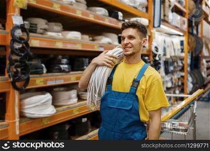 Male builder with coil of wires in hardware store. Constructor in uniform look at the goods in diy shop