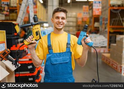 Male builder with power tools in hardware store. Constructor in uniform look at the goods in diy shop