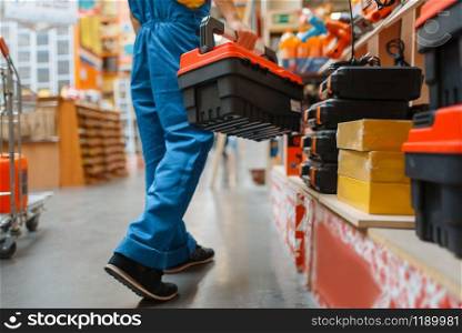 Male builder with toolbox at the shelf in hardware store. Constructor in uniform look at the goods in diy shop