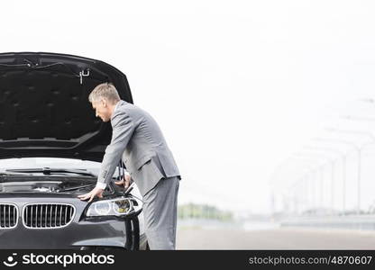 Male business executive looking at breakdown car against sky