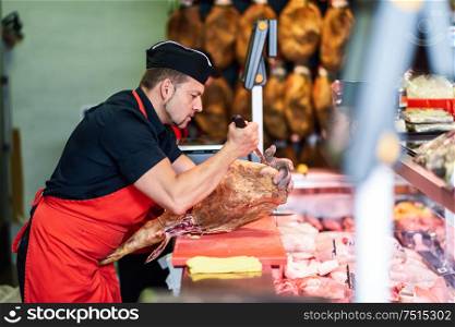 Male butcher boning a ham in a modern butcher shop. Butcher boning a ham in a modern butcher shop