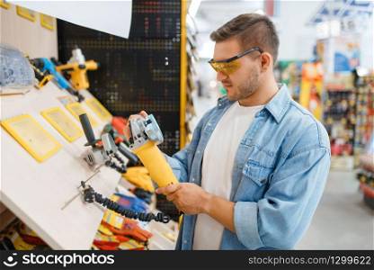 Male buyer holding edging machine in hardware store. Customer look at the goods in diy shop, shopping in building supermarket. Buyer holding edging machine in hardware store