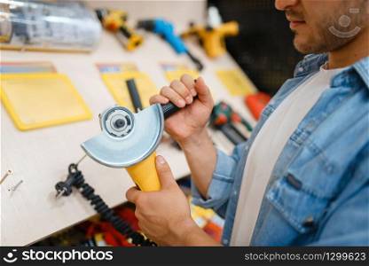 Male buyer holding edging machine in hardware store. Customer look at the goods in diy shop, shopping in building supermarket