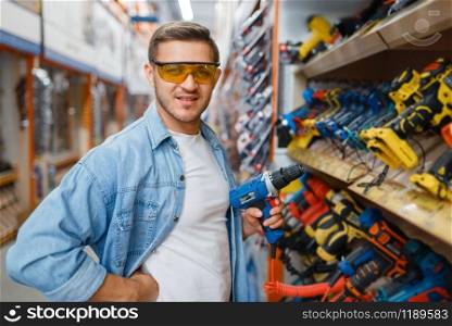 Male buyer holding electric screwdriver in hardware store. Customer look at the goods in diy shop, shopping in building supermarket