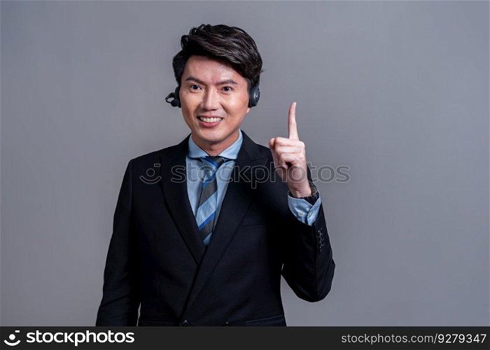 Male call center operator wearing headset and formal suit standing confidently with finger pointing up gesture for product advertisement or HR recruitment on isolated background. Jubilant. Male call center operator wearing headset making finger pointing. Jubilant