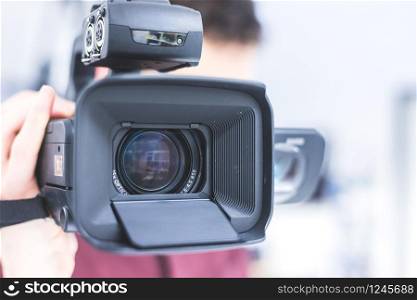 Male cameraman is holding a professional video camcorder, blurry background