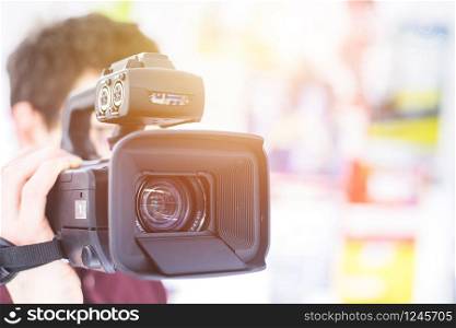 Male cameraman is holding a professional video camcorder, blurry background