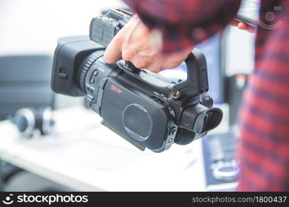 Male cameraman is holding a professional video camcorder, blurry background