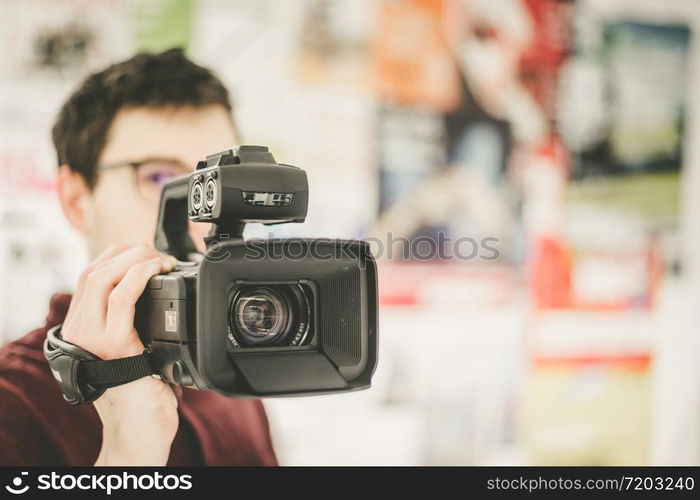 Male cameraman is holding a professional video camcorder, blurry background