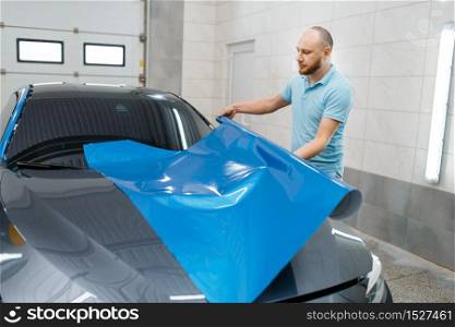 Male car wrapper holds protective vinyl foil or film roll. Worker makes auto detailing. Automobile paint protection coating, professional tuning. Car wrapper holds protective foil or film roll