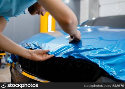 Male car wrapper puts protective vinyl foil or film on hood. Worker makes auto detailing. Automobile paint protection coating, tuning. Car wrapper puts protective foil or film on hood