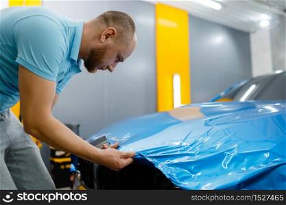 Male car wrapper puts protective vinyl foil or film on hood. Worker makes auto detailing. Automobile paint protection coating, tuning. Car wrapper puts protective foil or film on hood