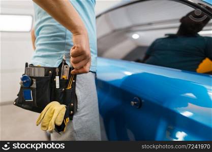 Male car wrapper with tool belt installs protective vinyl foil or film on vehicle wrapping. Worker makes auto detailing. Automobile paint protection coating, professional tuning. Car wrapper with tool belt, protection coating