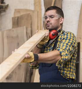 male carpenter seriously looking wooden plank