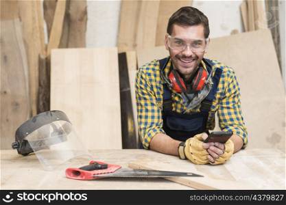 male carpenter standing workbench using mobile phone
