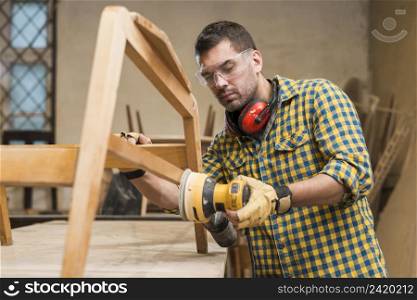 male carpenter wearing safety glasses using sander furniture workshop