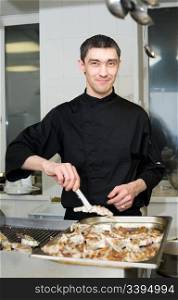 male caucasian chef in black uniform grills lamb ribs at restaurant kitchen