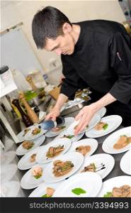 male caucasian chef in black uniform pour sauce on plates with lamb meat