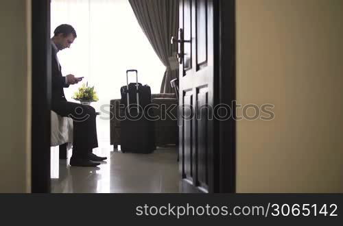 Male caucasian manager texting with mobile phone in hotel room during business trip. Dolly shot