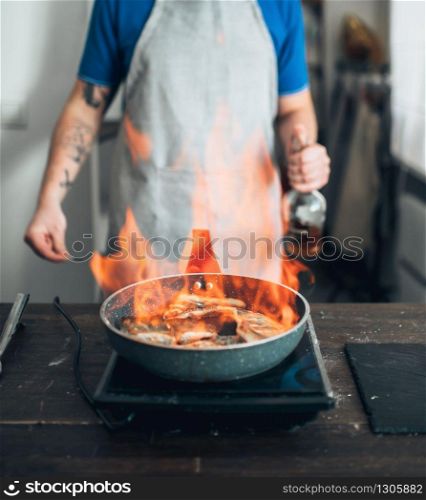 Male chef against frying pan with fire, cooking sea bass fish fillet. Seafood preparation. Chef against frying pan with fire, fish cooking