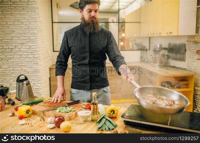 Male chef cooking meat with vetables into the frying pan on the kitchen. Man preparing beef. Male chef cooking meat with vetables into the pan
