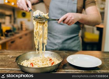 Male chef cooking pasta, pan on wooden kitchen table. Homemade fettuccine preparation process. Traditional italian cuisine