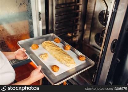 Male chef hands puts apple strudel on metal baking sheet in the oven. Sweet bakery, dessert preparation