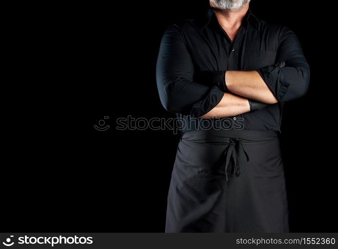 male chef in black uniform crossed his arms in front of his chest on a black background, banner for restaurants and cafes, empty space for an inscription