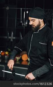 Male Chef in black uniform sharpening the knives in the kitchen.
