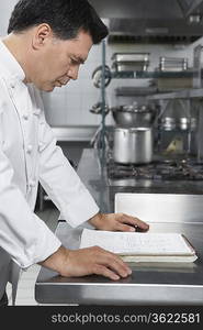 Male chef reading recipe book in kitchen