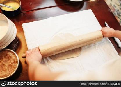 Male chef roll out the dough with a rolling pin, top view, wooden kitchen table on background. Homemade strudel cooking