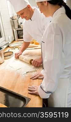 Male chef rolling dough with rolling pin assistant watching