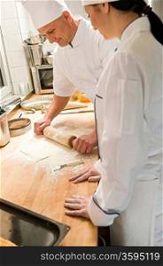 Male chef rolling dough with rolling pin assistant watching