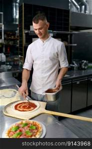 Male chef spreading tomato paste on pizza base. Traditional Italian dish baking process by delicious recipe. Male chef spreading tomato paste on pizza base