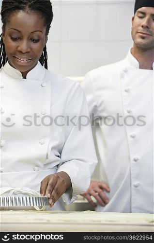 Male chef watching female chef preparing food in kitchen