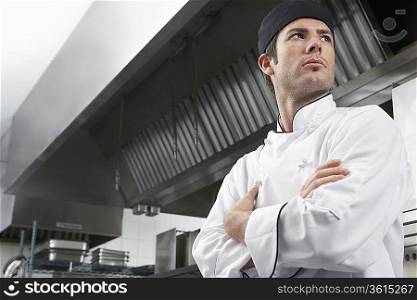 Male chef with arms crossed in kitchen, low angle view