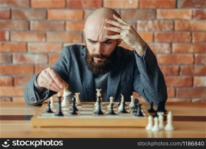 Male chess player understood that he lost, checkmate. Chessplayer at board, front view, intellectual tournament indoors. Chessboard on wooden table, strategy game. Chess player understood that he lost, checkmate