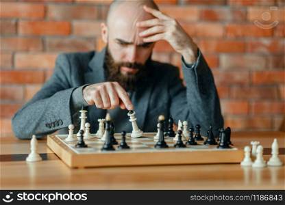 Male chess player understood that he lost, checkmate. Chessplayer at board, front view, intellectual tournament indoors. Chessboard on wooden table, strategy game