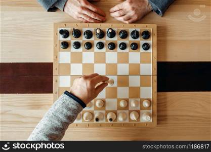 Male chess players at board, move of white, top view. Two chessplayers begin the intellectual tournament indoors. Chessboard on wooden table