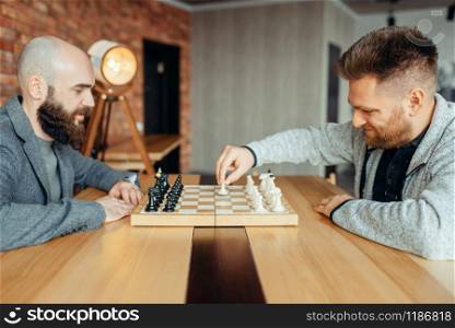 Male chess players begin playing, the first move. Two chessplayers begin the intellectual tournament indoors. Chessboard on wooden table, strategy game