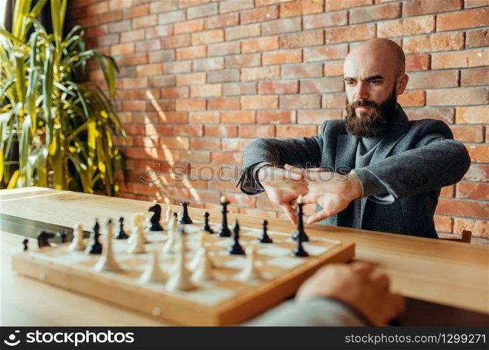 Male chess players on competition, board with figures. Two chessplayers begin the intellectual tournament indoors. Chessboard on wooden table, strategy game