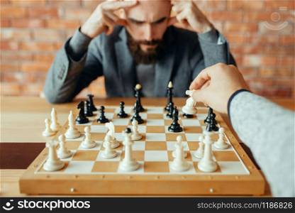 Male chess players playing at board, white knight move. Two chessplayers begin the intellectual tournament indoors. Chessboard on wooden table