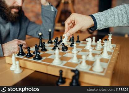 Male chess players playing at board, white knight takes pawn. Two chessplayers begin the intellectual tournament indoors. Chessboard on wooden table