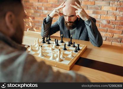Male chess players playing, thinking process. Two chessplayers begin the intellectual tournament indoors. Chessboard on wooden table, strategy game. Male chess players playing, thinking process