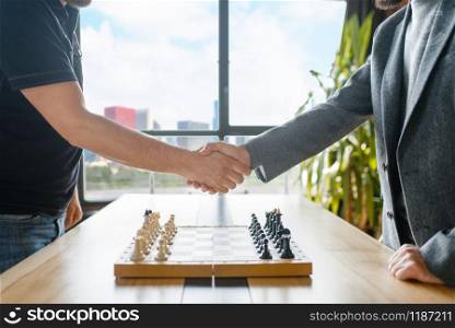 Male chess players shake hands before the game. Two chessplayers begin the intellectual tournament indoors. Chessboard on the table. Male chess players shake hands before the game