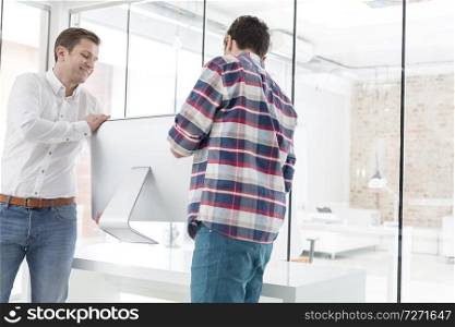 Male colleagues carrying desktop computer in office