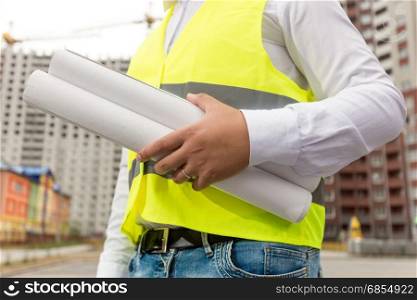 Male construction engineer with rolled blueprints at building site