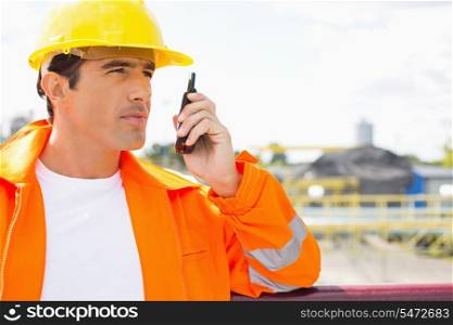 Male construction worker communicating on walkie-talkie at site