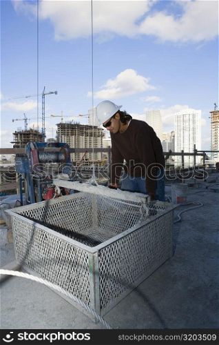 Male construction worker leaning against a basket at a construction site